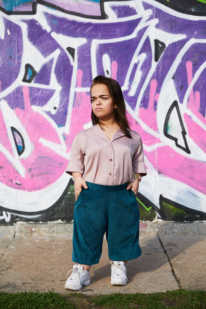 woman with dwarfism in front of grafitti wall wearing matching rose blouse and turquoise pants