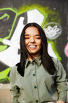 woman with dwarfism smiling in front of grafitti wall, wearing green blouse