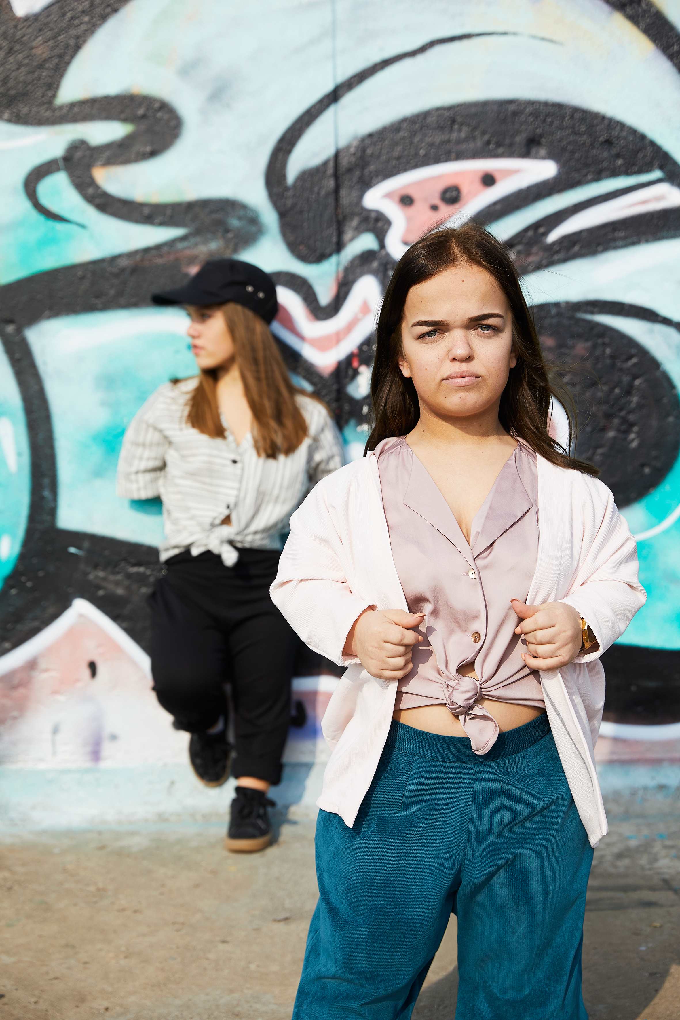 two woman with dwarfism modelling in front of grafitti wall