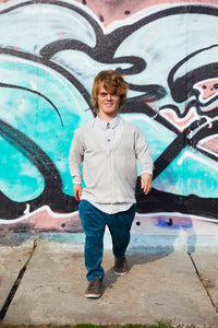 man with dwarfism in front of grafitti wall smiling wearing tailored clothes