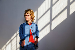 male model with dwarfism leaning against wall wearing blue college jacket