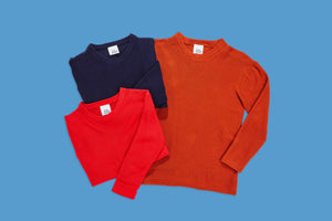 set of rusty red pullover next to folded up blue and bright red pullover