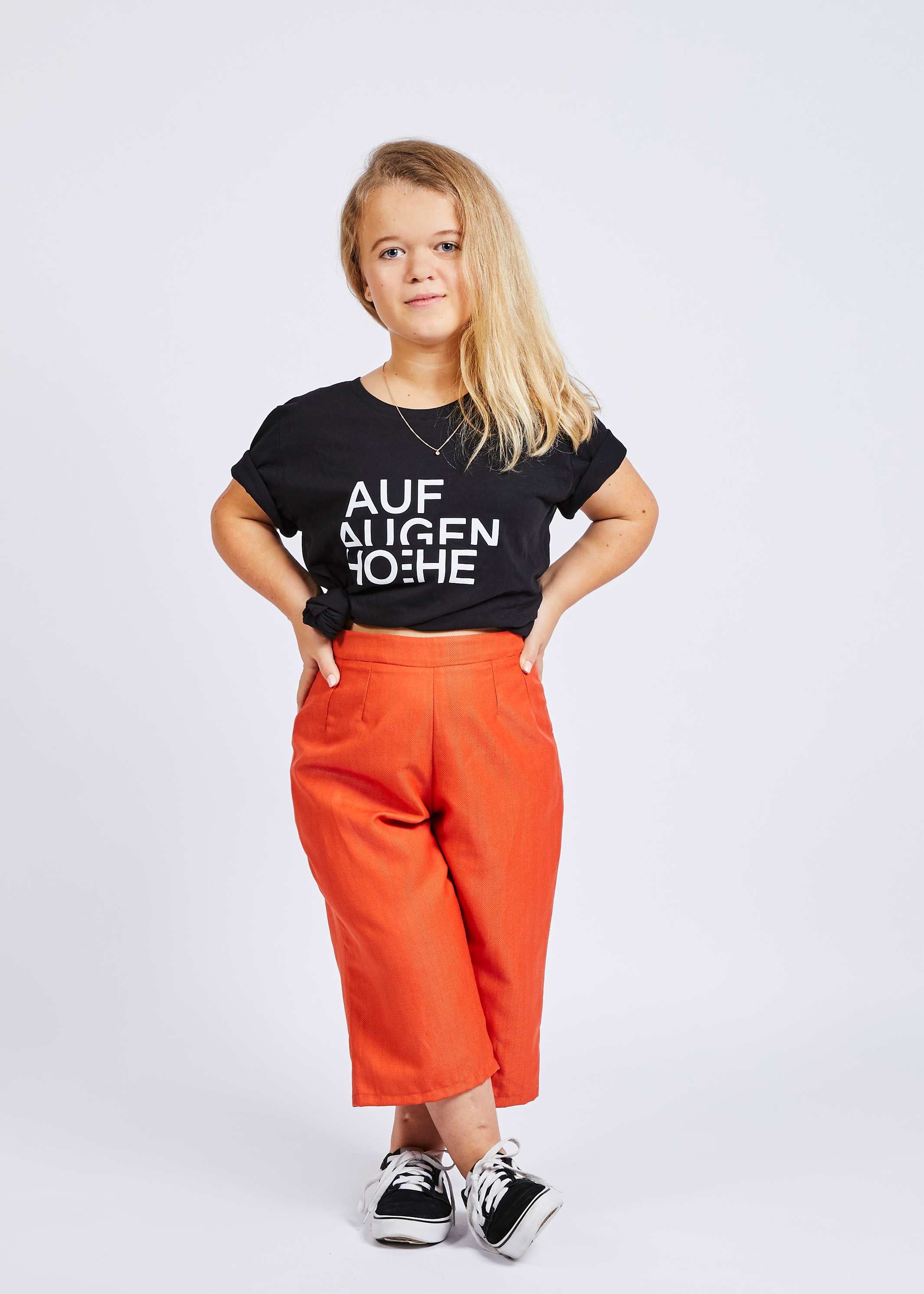 woman with dwarfism wearing red culotte pants and black t-shirt